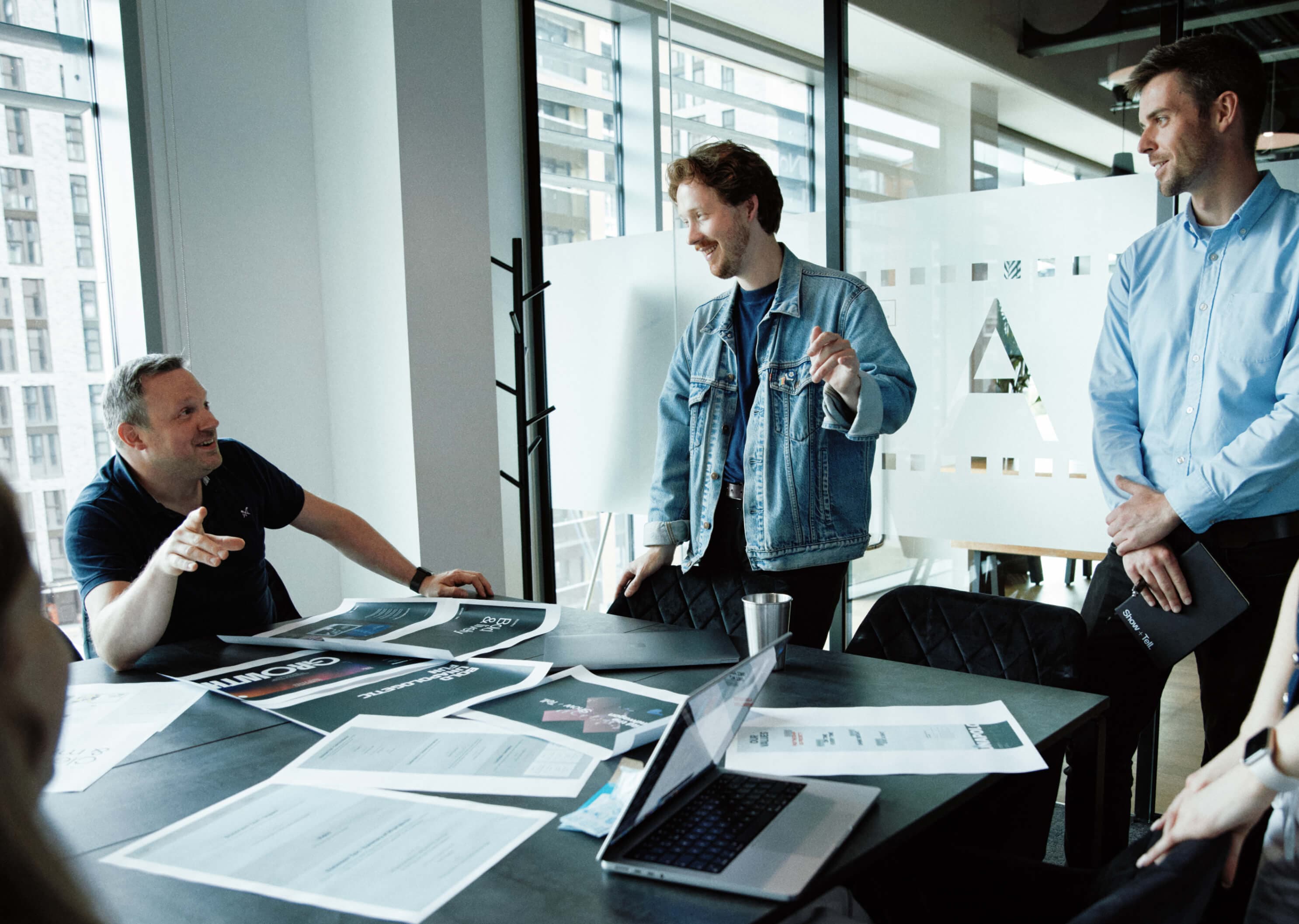 Team member enthusiastically presenting creative work to a small, focused group in a relaxed workspace.