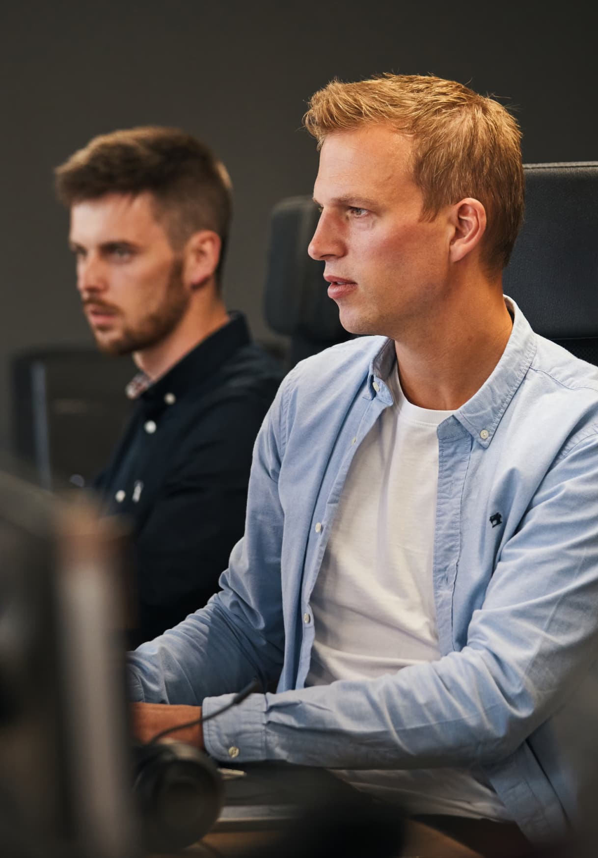 Team members seated at a shared desk, focused on their individual tasks in a modern office environment.